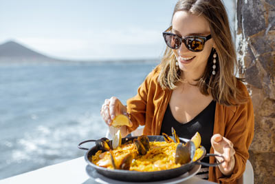 A woman eating paella by the sea